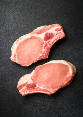 Raw pork meat steaks on black background. Flat lay with copy space.