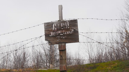 An old sign that says STAY AWAY from the area among the fall trees on a rainy overcast day in late fall.