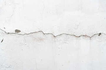 Close up of old white plaster wall with large crack and peeling texture
