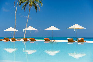 Obraz na płótnie Canvas Stunning luxury resort infinity pool with lounge sunbeds and umbrellas, palm trees and sea view reflections, tropical island paradise perfect for summer vacation and exotic travel. Tourism wall art