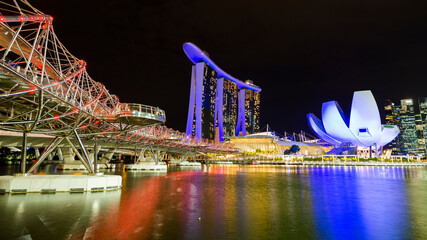 Naklejka premium Singapore Marina Bay at night with Marina Bay Sands and Merlion Park illuminated, attracting crowds of visitors, symbolizing tourism economy and vibrant city life.