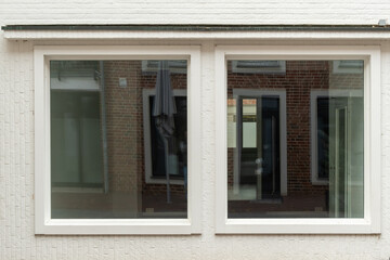 Two windows reflecting brick building and parasol on white wall