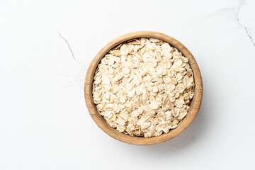 Rolled oats or oat flakes in a wooden bowl on white background. Top view.