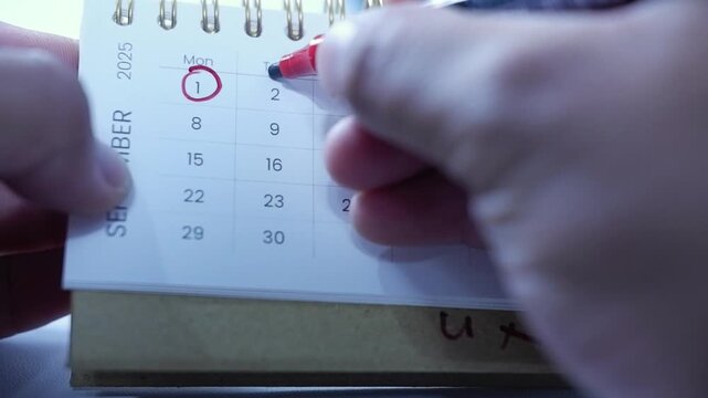 A person marks a calendar with a red marker, circling dates and marking deadlines and progress. Time management, planning, scheduling Important days, Deadlines
