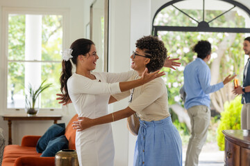 Bride in white dress hugging friend warmly at home during wedding celebration