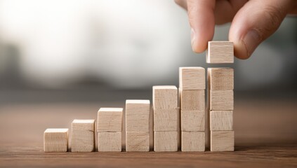A hand places a wooden block on a growing stack of blocks