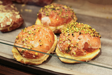 Sweet bakery buns with pistachio topping. Fresh pastry dessert with sugar glaze. Delicious sweet rolls on tray in bakery shop. Traditional pastry with nuts decoration. Appetizing homemade sweet bread.