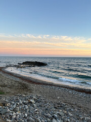 A gentle sunset illuminates the sandy-pebble beach, waves roll onto the shore, a gradient sky with soft clouds. Spain, 2022.