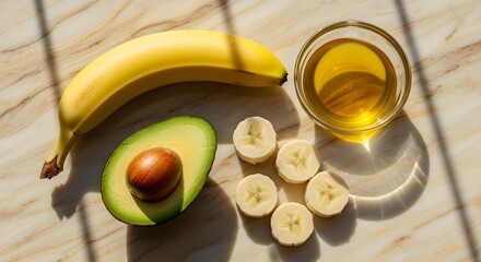 A top-down shot showcases avocado halves, sliced banana, and a bowl of oil on a marble surface, perfect for healthy eating concepts.