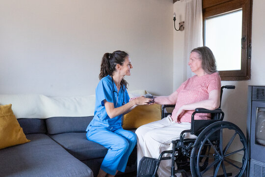 Nurse checking blood pressure of senior woman in wheelchair at home