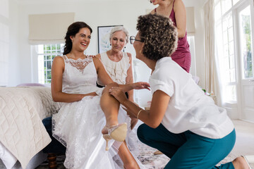 Fototapeta premium Bride laughing with friends helping her with wedding dress in bedroom