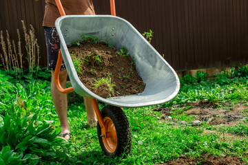 A man is emptying soil from a garden cart in the garden.