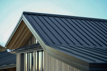Fototapeta premium A stylish metal roof with sharp lines complements large glass windows on a modern structure illuminated by soft evening light