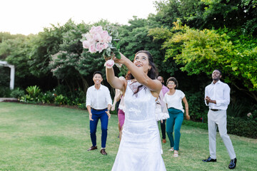 Bride joyfully tossing bouquet to excited guests in lush garden setting