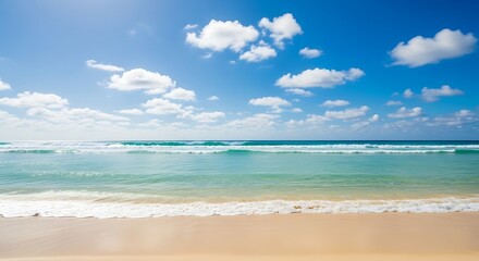 Fototapeta premium Sunlit sandy shore with gentle ocean waves under a cloudy blue sky.