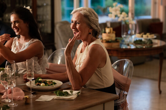Elderly woman joyfully toasting at wedding reception, enjoying dinner with family - Powered by Adobe