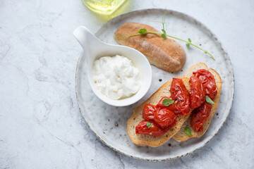 Plate with roasted tomato bruschettas and stracciatella cheese, horizontal shot on a white stone background, high angle view