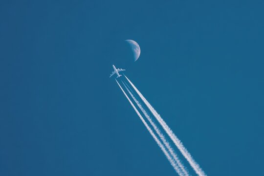 Airplane trails across a vast blue sky with a crescent moon - Powered by Adobe