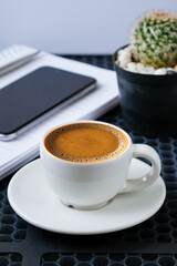 Hot Espresso Coffee with Smartphone, Notebook, and Cactus Plant on Table