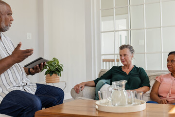 African American man discussing with senior women on couch at home, holding tablet