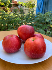 Red apples on white plate outdoors, vibrant contrast and natural freshness evoke cozy, rustic atmosphere