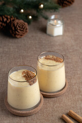 Two glasses of classic eggnog with cinnamon powder and a cinnamon stick on the side, ready to be enjoyed during the holidays