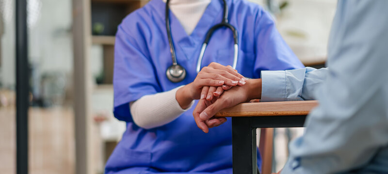 Young nurse caring patient with hand support, compassionate healthcare worker offering comfort and reassurance in clinic setting