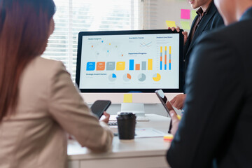 Team meeting analyzing colorful business charts and graphs on desktop monitor with smartphones and coffee creating focused collaborative energy