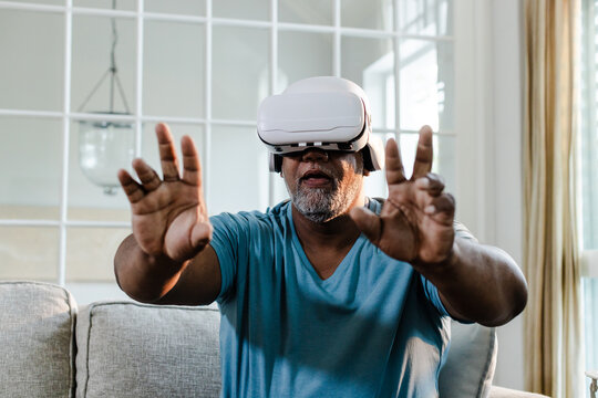 African American man using VR headset on sofa, exploring virtual reality experience