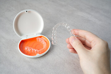 Clear dental aligner in hand and orange case on table. Dental orthodontic mouthpiece.