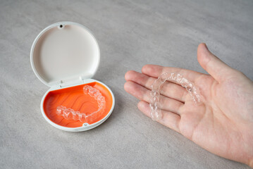 Clear dental aligner in hand and orange case on table. Dental orthodontic mouthpiece.