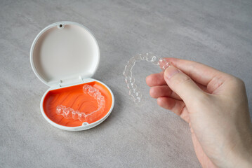 Clear dental aligner in hand and orange case on table. Dental orthodontic mouthpiece.