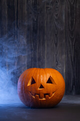 Bright orange Halloween pumpkin with carved face, surrounded by mist, set against a dark wooden background, creating a spooky and festive atmosphere for seasonal celebrations
