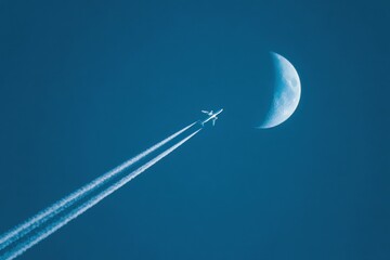 Airplane trails into a night sky with a crescent moon