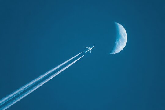 Airplane trails into a night sky with a crescent moon