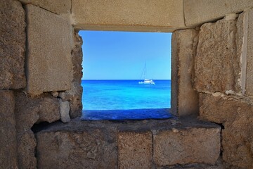 Sea view from ancient wall, travel and vacation concept. Turquoise sea with sailboat, summer holiday, stone window to the ocean sea.  Rhodes Island Greece, Fortress in the old town.
