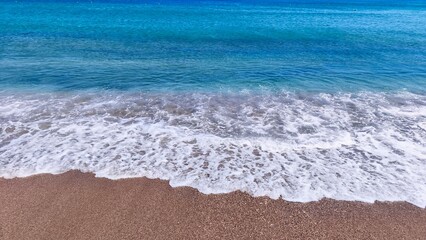 Crystal clear turquoise sea waves gently rolling onto a sandy beach. Idyllic summer coastal scene...