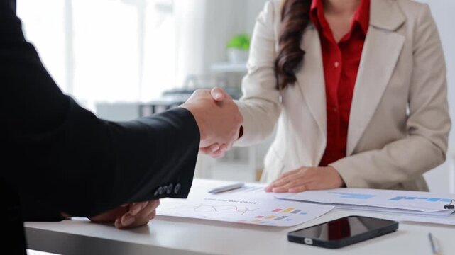 Professional businesspeople shaking hands at sleek office desk, celebrating successful partnership and collaborative agreement with genuine enthusiasm