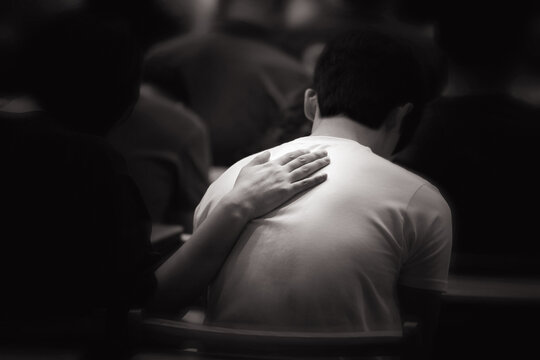 A Christian who places his hands on the backs of people in despair during prayer time, comforts them, and prays with tears in his eyes.
