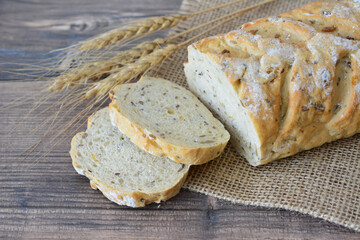 Sliced loaf of bread with wheat stalks on wooden surface