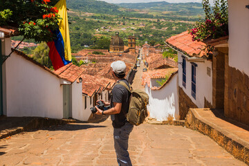 Young Latino man with backpack and camera exploring the colonial streets of Barichara, Colombia, enjoying cultural tourism, photography, travel adventure, discovery and authentic lifestyle abroad.