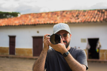 Latino man with camera taking a photo in the colonial town of Barichara, Colombia, showing lifestyle of travel photography, creativity, tourism, exploration, culture, discovery and authentic adventure