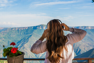 Young Latina woman enjoying music on headphones while facing scenic Colombian mountains