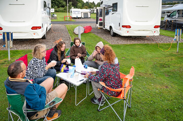 Family group enjoying breakfast at a campsite sitting around a table outdoors surrounded by caravans, including seniors and teenagers in a relaxed vacation atmosphere
