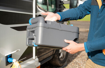 Person holding portable cassette toilet tank after removal from camper van during sanitation routine