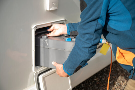 Person placing cassette toilet waste tank into camper van compartment during outdoor sanitation routine