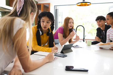Teens collaborating on school project at home, using tablet and taking notes