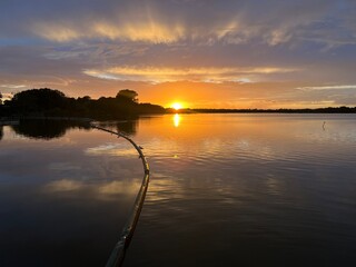 Summer sunset landscape sun setting over Norfolk Broads England uk tranquil water with the beautiful orange yellow blue skies viewed from sailing boat to horizon and trees reeds, clouds reflected 