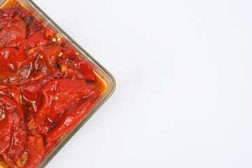 An overhead shot shows roasted red Macedonian peppers soaking in oil in a glass dish with plenty of copy space on a white background