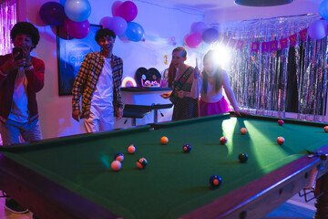 Naklejka premium Teens celebrating birthday playing pool in festive room with colorful balloons